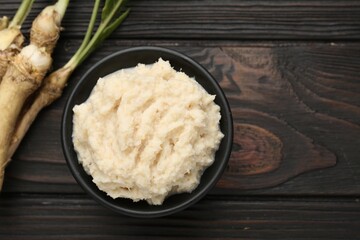 Tasty horseradish sauce and roots on black wooden table, flat lay. Space for text