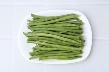 Fresh green bean pods on white tiled table, top view