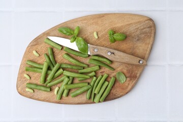 Cut green bean pods, basil and knife on white tiled table, top view