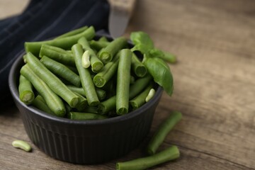 Pieces of fresh green beans in bowl on wooden table, closeup. Space for text