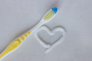 Flat lay composition with heart shape made of toothpaste and  toothbrush  on white background. The concept is dental and oral care products.
