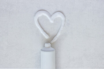 Flat lay composition with heart shape made of face cream on white background. The concept is skin, dental and hair care products.