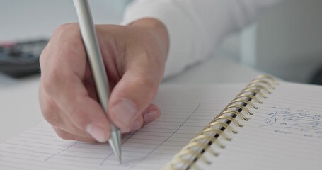 Close-up of hands - a man in a shirt draws and fills a table with a pen in a notepad on a metal spring on an office desk - Powered by Adobe