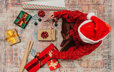 woman in hat sits on cozy rug surrounded gift boxes, wrapping Christmas presents