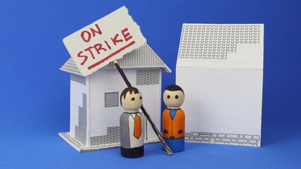 Strike written on a protest sign with a blue background. Demonstration among houses and cartoon men.