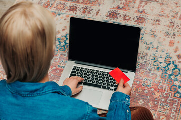 woman sitting on a carpet with a laptop, completes an online purchase.