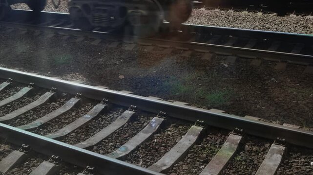 A view from a train window of a railroad siding with sleepers and a train passing in the background. A train's wheels are moving along the rails. Copy space for text