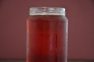 A close-up of a glass jar filled with a cold, red beverage, its surface covered in refreshing condensation droplets