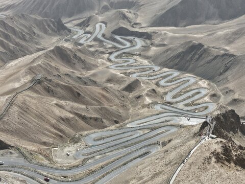 Aerial view of a serpentine road winding through rugged, arid mountains, a testament to human engineering against the stark landscape, Panlong Ancient Road, China.