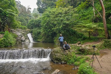 Fototapeta premium Two Adventurous Friends Capturing Moment While Explore Lush Jungle Waterfall