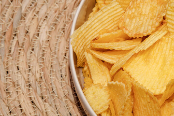 Close-up of a bowl filled with crispy golden chips. The ridged texture and crunchy look make them a classic salty snack. Placed on a woven natural mat for a rustic background. Selective focus.