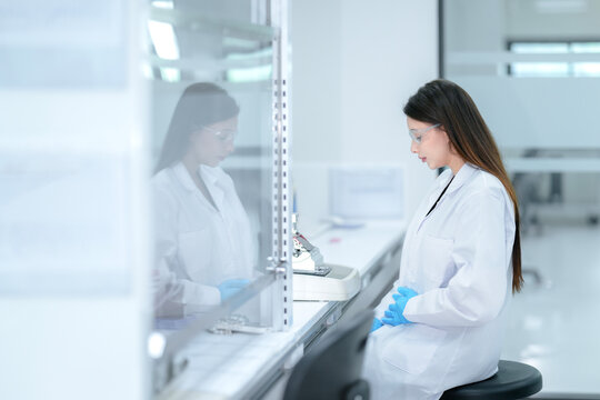A pharmaceutical technician performs aseptic compounding inside a sterile biosafety cabinet, preparing a cell culture for biologic drug development under strict quality control conditions.