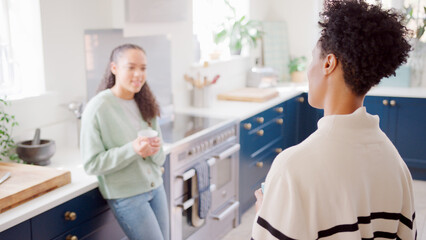 Fototapeta premium Mature Mother Talking With Teenage Daughter At Home In Kitchen Drinking Hot Drinks Together