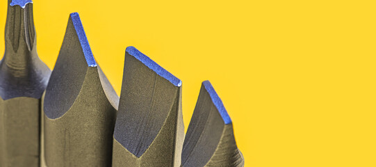 Macro photograph of various screwdriver bits with sharp metallic edges on yellow background. The...