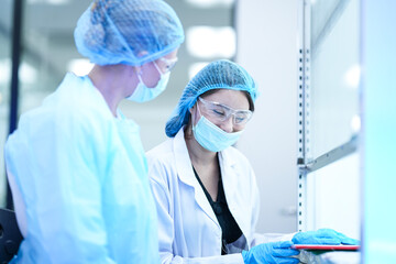 Two researchers in a GMP compliant cleanroom discuss experimental data. They are collaborating to troubleshoot a procedure in a pharmaceutical or biotechnology R and D facility.