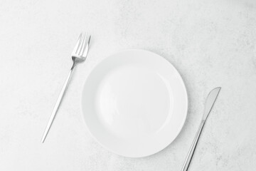 Simple dining setup with empty plate, fork, and knife on white surface