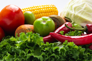Assortment of fresh vegetables including corn, tomatoes, carrots, green tomatoes, red chili peppers, cabbage, and lettuce isolated on white background