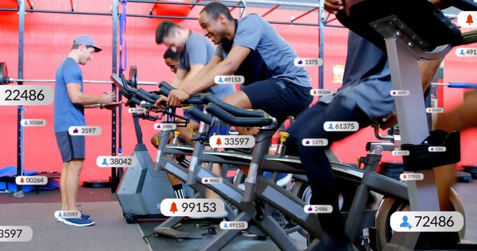 Cyclists adjusting seats and pedaling by red gym wall, trainer monitoring counts as metrics rising