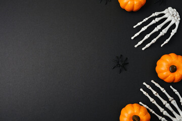 Orange pumpkins and white skeleton hands with black spiders on a dark background Halloween