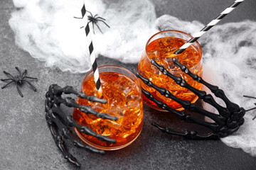 Halloween spooky drinks with ice and creepy skeleton hands on dark background