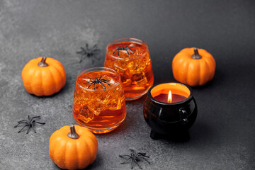 Orange pumpkin drinks with spiders and lit cauldron candle on dark background.