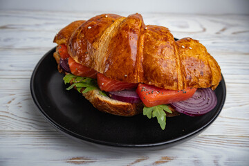 Croissant sandwich with salmon, arugula and blue onion on a white background