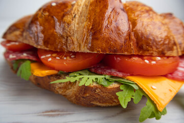 Croissant sandwich with cheese, meat and arugola on white wooden table