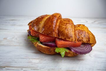 Croissant sandwich with salmon, arugula and blue onion on a white background