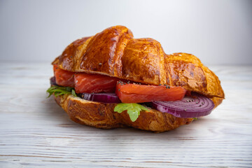 Croissant sandwich with salmon, arugula and blue onion on a white background