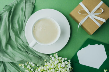 Top view of coffee cup, card and gift with spring lily of the valley bouquet