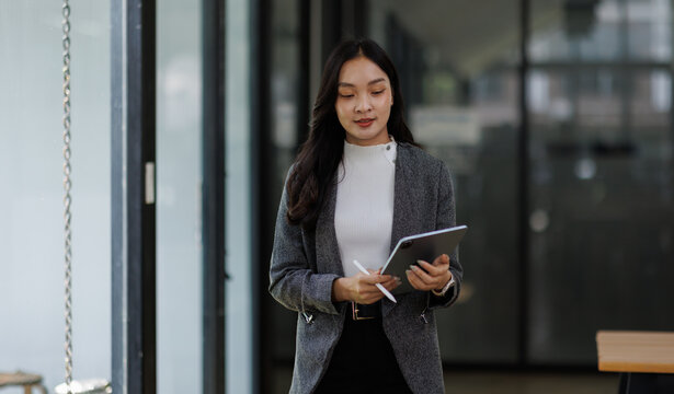 professional business asian woman looking at camera and smiling. businesswoman CEO holding digital tablet phone using fintech tab application standing at workplace in office.
