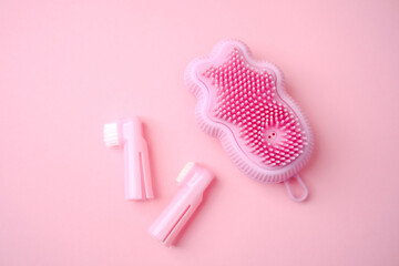 Pink dog paw bath brush and finger toothbrushes for pet cleaning on a pastel background.