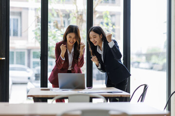 Two excited happy Young Asian businesswomen discuss with new startup project Idea presentation, analyze planning and financial statistics and investment market at office.
