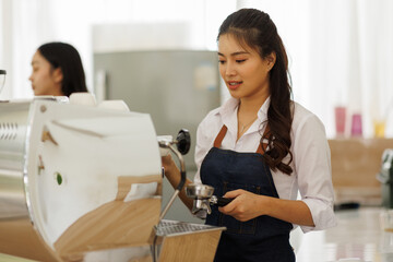 Two asian smiling young multinational waitresses wearing aprons using computer terminal while working in cafe

