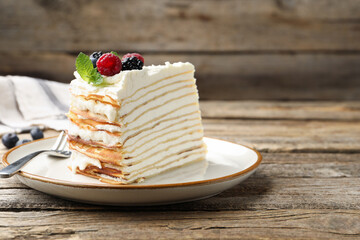 Piece of tasty crepe cake with berries served on wooden table, closeup. Space for text