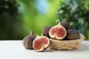 Fresh ripe figs in wicker basket on white wooden table outdoors, closeup. Space for text