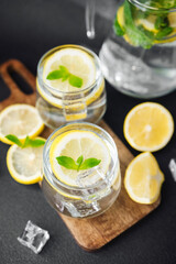 Citrus lemonade with fresh mint leaves and ice cubes in glass jug on bright table in sunny summer kitchen