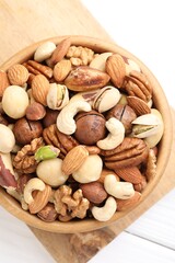 Mix of different nuts in bowl on white wooden table, top view