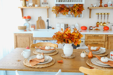 Autumn dining table setting with pumpkins and maple leaf bouquet. Natural wood surface.