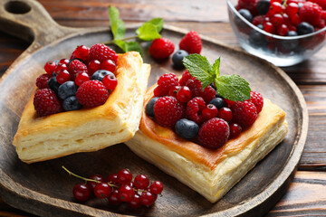 Tasty puff pastries with berries and mint on wooden table, closeup