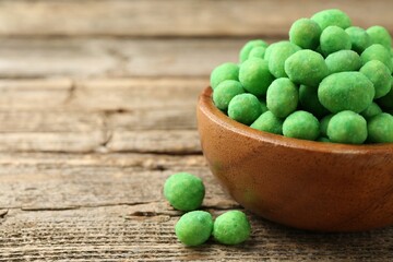 Delicious wasabi coated peanuts in bowl on wooden table, closeup. Space for text