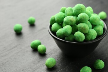 Delicious wasabi coated peanuts and bowl on dark textured table, closeup