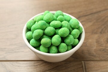 Delicious wasabi coated peanuts in bowl on wooden table, closeup