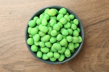 Delicious wasabi coated peanuts in bowl on wooden table, top view
