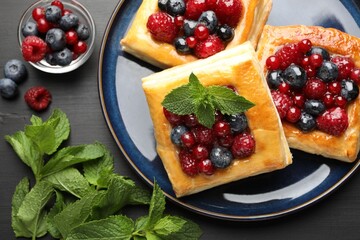 Tasty puff pastries with berries and mint on grey wooden table, flat lay