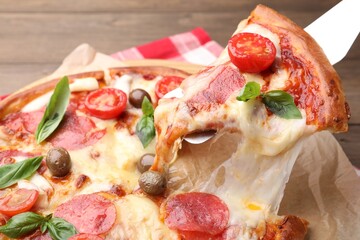 Taking piece of delicious pizza with cheese, salami, tomatoes and olives at table, closeup