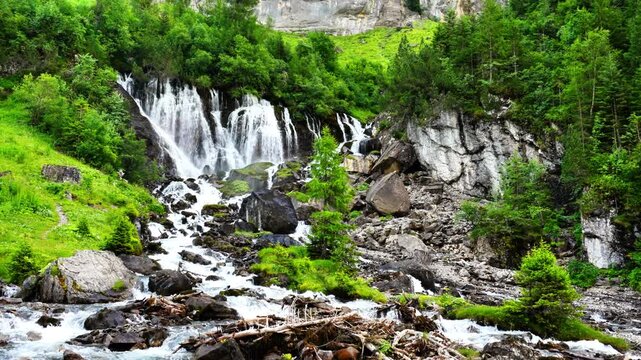 Waterfalls flow through Lenk Sibenf&auml;lle in Switzerland, surrounded by lush green forest, moss-covered rocks, and cascading streams in a dramatic alpine mountain landscape of natural beauty