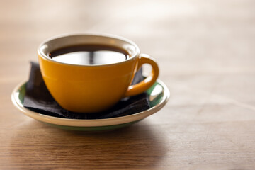 A warm yellow coffee cup sits on a green-rimmed saucer with a black napkin, close up