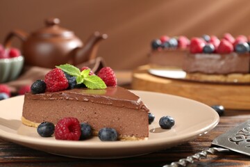 Piece of tasty chocolate cheesecake with berries served on wooden table, closeup