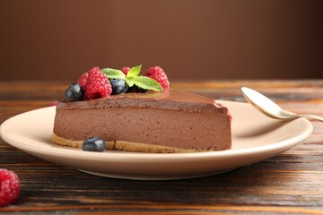 Piece of tasty chocolate cheesecake with berries on wooden table, closeup